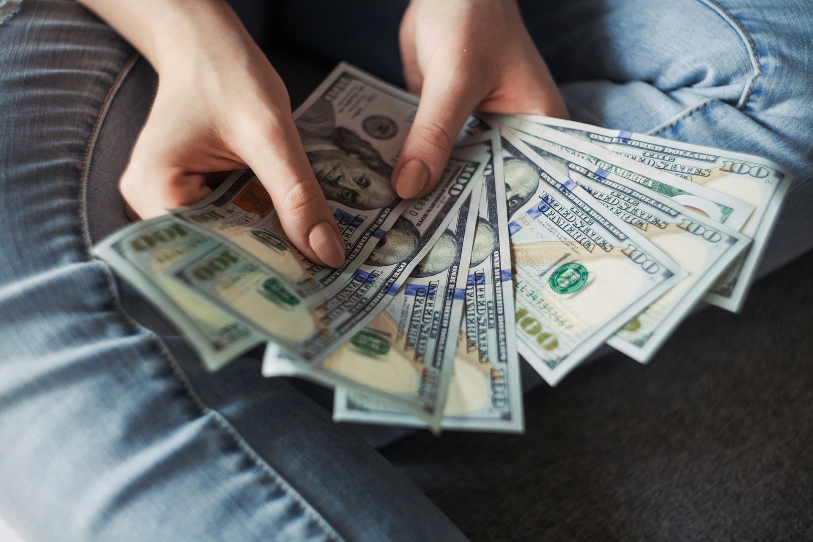 Person fanning out one-hundred dollar bills, representing payroll being paid out